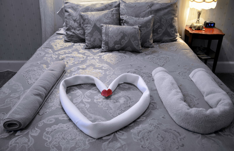 Romantic Retreat Suite awaits with I heart you spelled out on the bed by the towels.